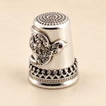 Sterling silver swallow thimble with marcasite and red garnet accents, photographed to show its decorative detailing.
