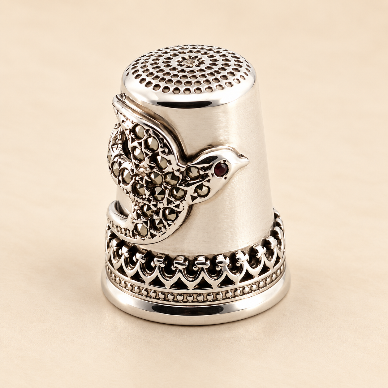 Sterling silver swallow thimble with marcasite and red garnet accents, photographed to show its decorative detailing.